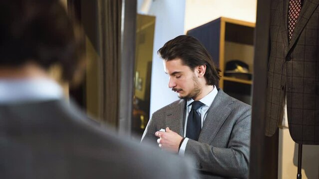 Young bearded man trying on suit in front of fashion boutique mirror.