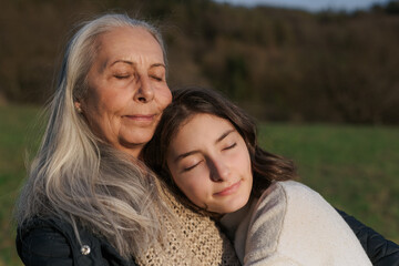 Happy senior grandmother with teenage granddaguhter hugging in nature on spring day.