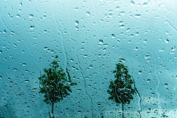 Car glass in drops and trickles of rain against dark blue sky and trees abstract background copy space