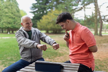 Happy senior father with his adult son with Down syndrome playing and sitting in park.