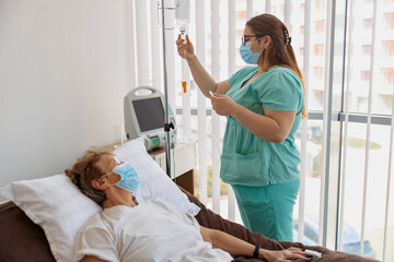 Nurse in mask controls drip of her patient during Covid-19 epidemic. High quality photo