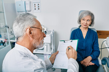 Grey-haired audiologist doing consultation for senior woman patient with hear problems at hearing center. Hearing doctor's consultation