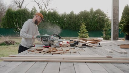 Man cutting wood using table saw on construction site of a modern wooden house. Man working on a house project outside at the sunset. Construction of Scandinavian barnhouse. High quality 4k footage