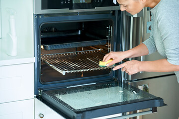 Young woman cleaning oven in the kitchen