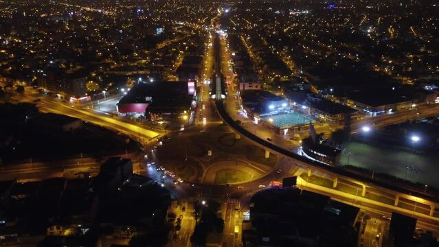 Drone night time video of a roundabout in Lima, Peru called "Ovalo Higuereta". Slowly flying forward while tilting camera down. Many city lights and car lights can be seen.