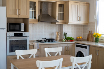 Kitchen with classic style interior. Wooden furniture, gas cooktop and separate electric wall oven, wooden utensil, fresh fruits and vegetables on marble tabletop. Copy space, background, close up.