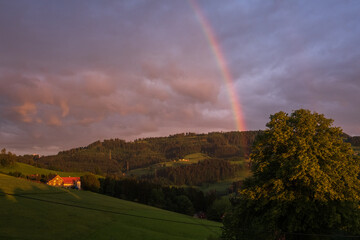 Regenbogen, der in den Wolken verschwindet in einer idyllischen Hügellandschaft.