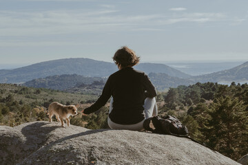 Young girl and her dog on a rock in the mountains, resting and looking at the scenery, in the...