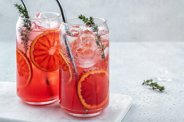 Blood Orange lemonade cocktail with ice and thyme on light gray concrete background