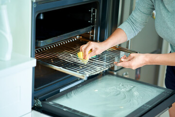 Young woman cleaning oven in the kitchen