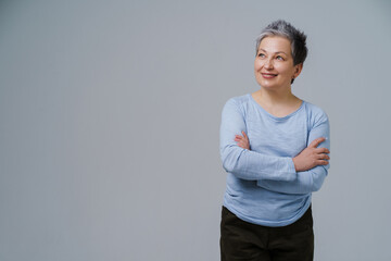 Mature grey hair woman posing with hands folded in blue blouse looking sideways up, copy space on left isolated on white background. Healthcare concept. Aged beauty concept. Copy space
