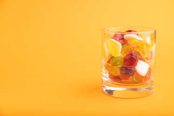 Various fruit jelly candies in drinking glass on orange background. copy space, side view.