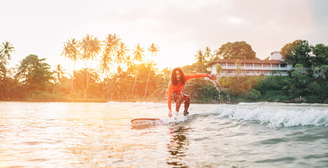 Black long-haired teen boy riding a long surfboard. He caught a  wave in an Indian ocean bay with...