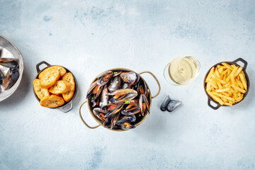 Cooked mussels with French fries and toasted bread, with a glass of white wine, top shot on a slate background with copy space