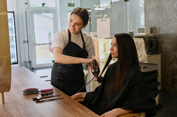 A female hairdresser makes styling hair for the beautiful young caucasian woman in a beauty salon