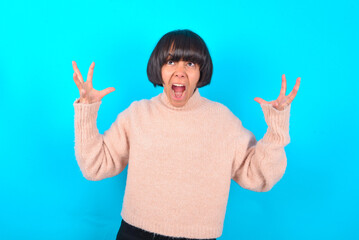 young brunette woman wearing pink knitted sweater over blue background crying and screaming. Human...