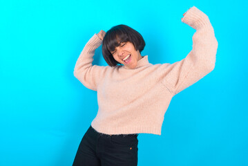 Yes I am winner. Portrait of charming delighted and excited young brunette woman wearing pink knitted sweater raising up fist in triumph and victory smiling achieving success grinning from delight.