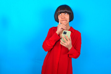 Image of a thinking dreaming young brunette woman with short hair wearing red shirt over blue...