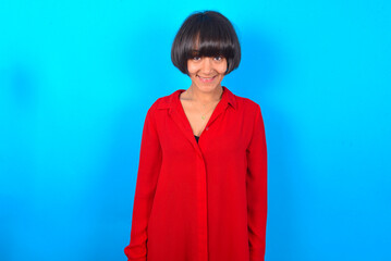Fototapeta premium young brunette woman with short hair wearing red shirt over blue background with nice beaming smile pleased expression. Positive emotions concept