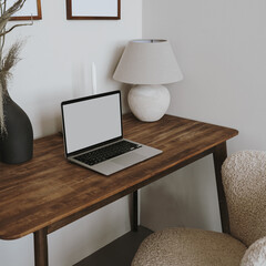 Laptop computer with blank screen on table with lamp and flowers bouquet. Aesthetic influencer boho...