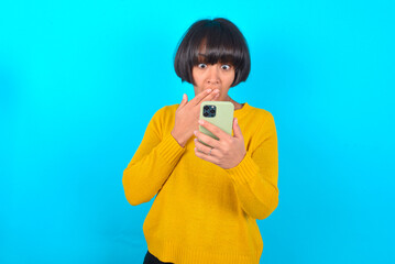 young brunette woman with short hair wearing yellow knitted sweater over blue background being...