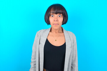 Stunned young businesswoman with bob haircut wearing blazer against blue wall stares reacts on...