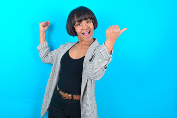 Hooray cool young businesswoman with bob haircut wearing blazer against blue wall point back empty...