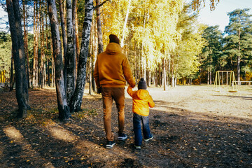 Father and son walking in autumn forest.