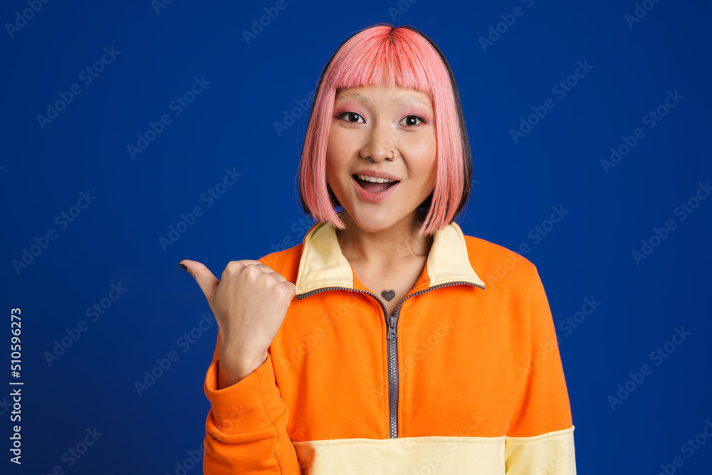 Wall mural Asian surprised girl with pink hair pointing finger aside