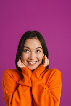 Young asian woman wearing sweater smiling and plugging her ears