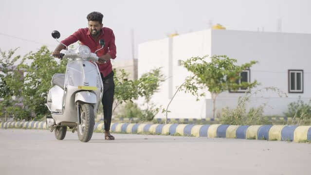 full shot of Worried young man pushing Ev or electric scooter on road druring travel due to low battery - concept of engine failure and breakdown.