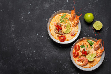 Tom Yum kung Spicy Thai soup with shrimp in a bowls on a black stone background, top view