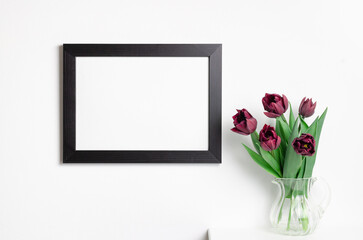 Blank black picture frame mockup on white wall with green plant
