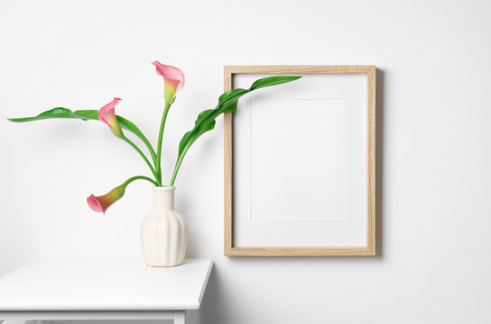 Empty wooden portrait frame mockup with calla flowers on white wall