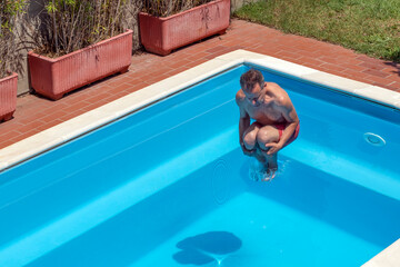 Top view of a caucasian man that takes a bomb dive in the swimming pool on a sunny day