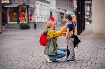 Young blond woman in raincoat and backpack give present toy to little preschooler girl on street