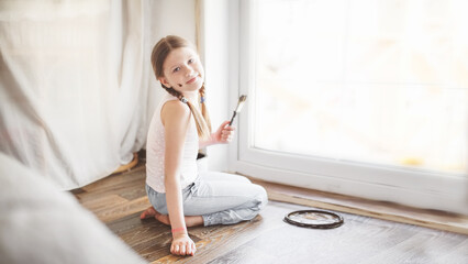 Kid girl with pigtails paints, covers a wooden board threshold with dark impregnation (oil), top...