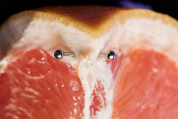 Half of grapefruit with vertical barbell piercing on a background.