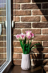 Spring flowers. Vase with tulips by the window. Brick wall