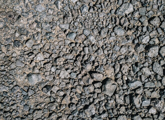 Dark grey cinder stones lie on a dirt road, top view in the rays of the midday sun.