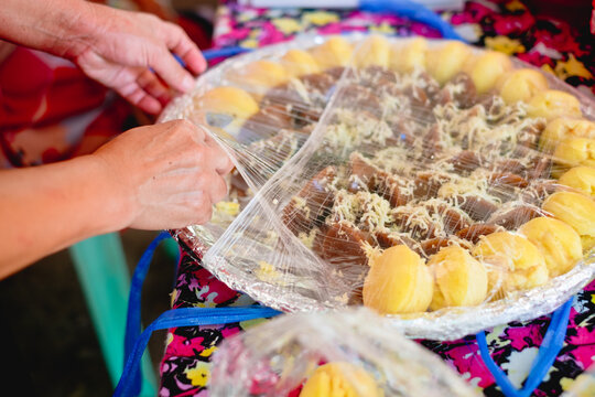 Hand getting a piece of sticky rice snacks or kakanin of Puto and Kutsinta in big winnowing basket covered by cellophane, a protection from contamination. Selective focus.