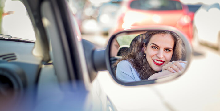 Reflection face of beautiful smiling girl standind in the car mirror.