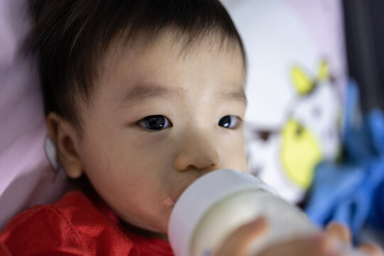 Portrait image of​ 1-2 years old​ child lying on bed with holding a milk bottle drinking milk