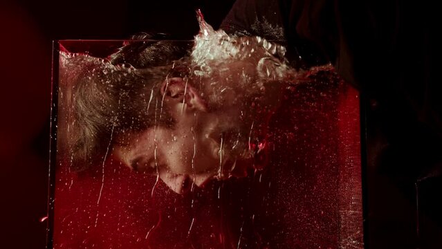 Portrait of a man immersing his face in water. Dark video with red light. Man screaming emotion underwater