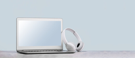 Laptop. Mockup screen and wireless headphones on white desk. plain blue background. Distant...