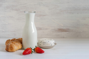 Jar of milk, fresh challah bread, ripe strawberries, soft cheese for Jewish holiday Shavuot over...
