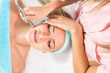 Naklejka premium Beautician therapist applying face treatment in beauty salon to young woman.