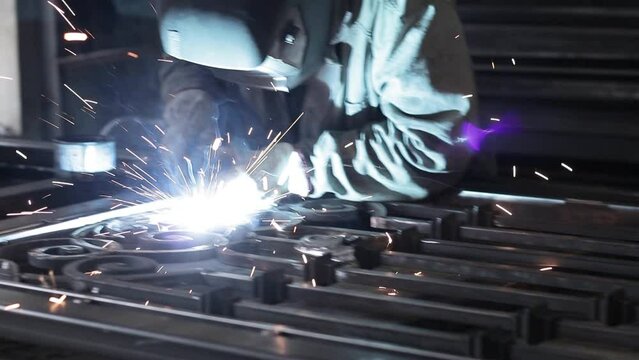 Professional male blacksmith forming red hot metal on an anvil in interior blacksmith workshop.