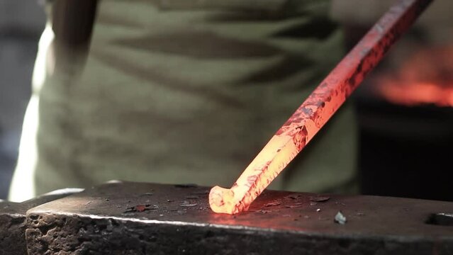 Professional male blacksmith forming red hot metal on an anvil in interior blacksmith workshop.
