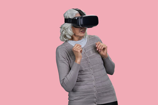 Frightened senior woman using virtual glasses standing on color background. People and modern technology concept.